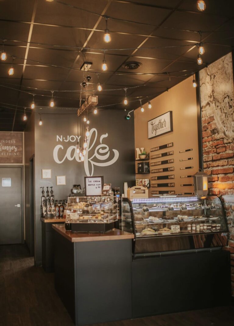 The inside of N-Joy Cafe, showcasing their logo and front counter displaying various desserts and artwork.