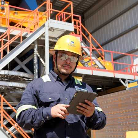 Engineer employee with a yellow hard hat working at Gerdau's steel mill with orange railings in the background.